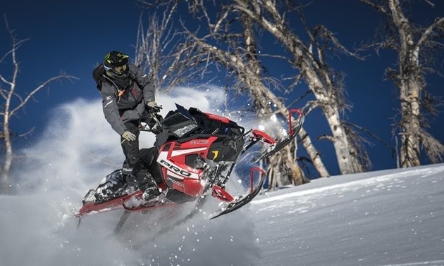 image of a man having fun driving a red polaris snowmobile in the mountains in winter