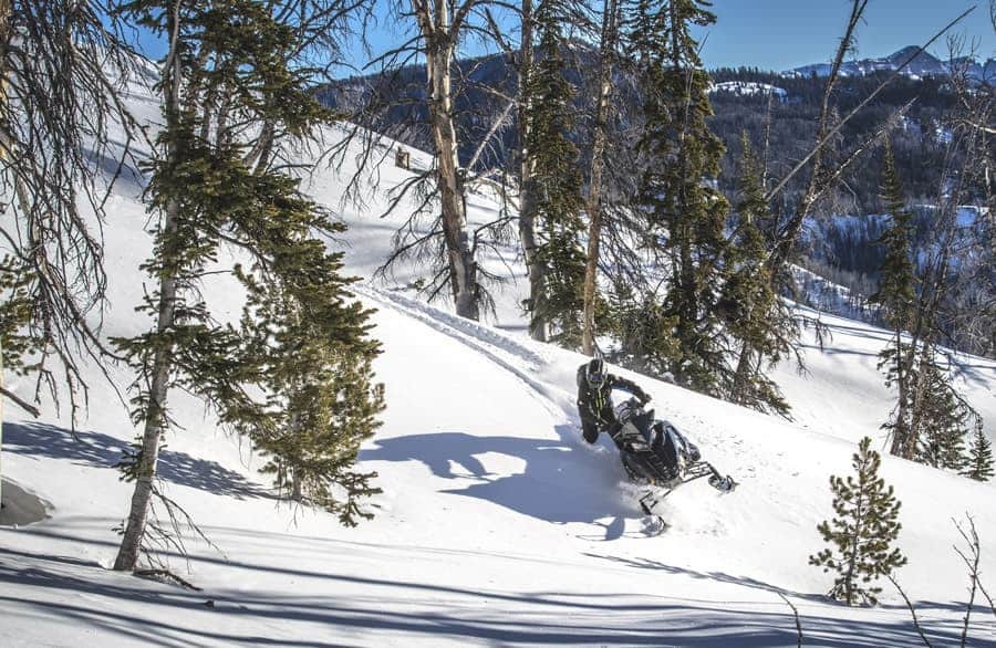 image of a man having fun driving a black polaris snowmobile in the mountains in winter