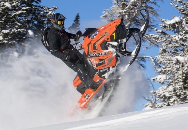 image d'un homme en habis sportif qui conduit sa nouvelle Polaris PRO-RMK orange sur les montagnes en hiver